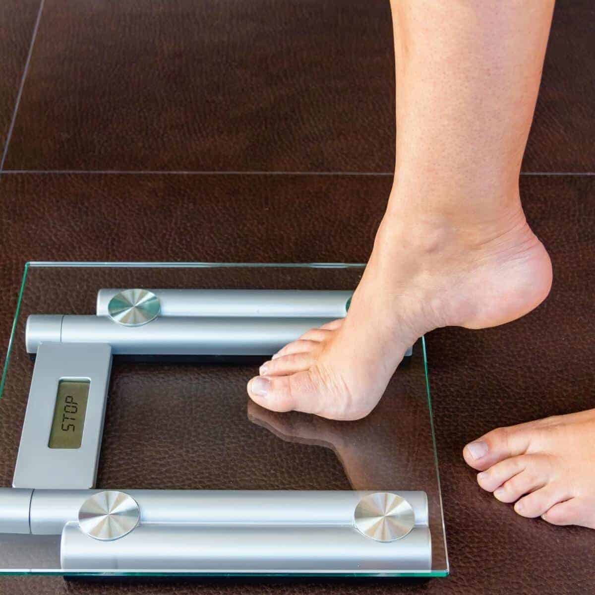 one foot hesitatingly stepping on bathroom scales which read the word STOP!