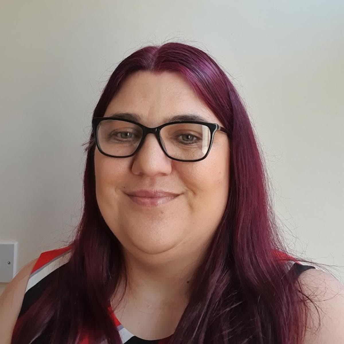 A head and shoulders photo of Jen, a woman in her 40's with deep red coloured hair and smiling at the camera
